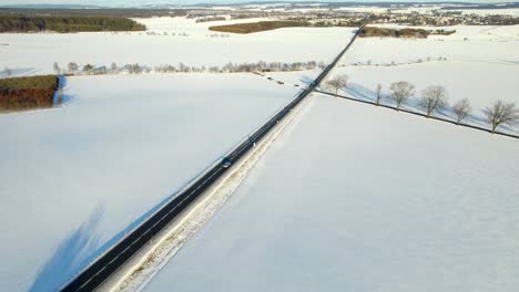Aerial-view-of-a-road-with-passing-cars-in-a-winter-landscape-covered-with-snow