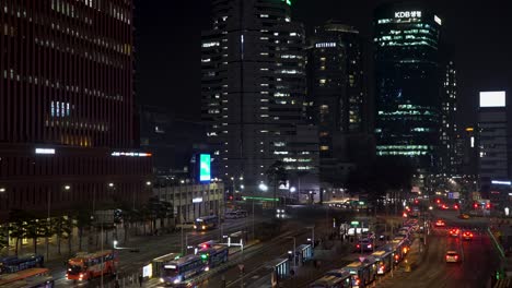 The-glow-of-downtown-Seoul,-South-Korea-looks-over-a-busy-bus-station-at-nighttime