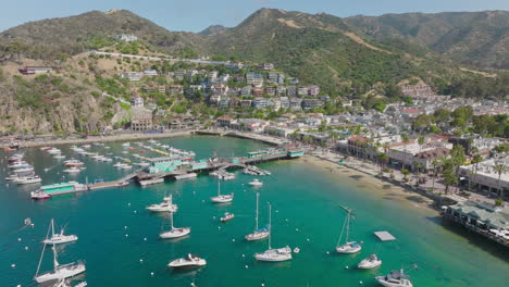 Aerial-Drone-Shot-of-Stunning-Clear-Catalina-Island-Harbor-on-Sunny-Day,-Boats-Docked-Below-and-Mountain-Terrain-in-Horizon