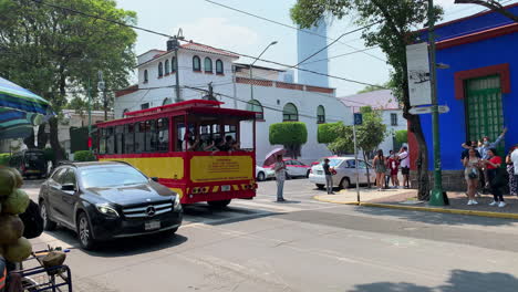 Der-Gelb-rote-Straßenbahn-Sightseeing-Bus-Fährt-An-Besuchern-Vorbei,-Die-Vor-Dem-Berühmten-Blauen-Haus-Des-Frida-Kahlo-Museums-Schlange-Stehen