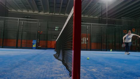 Padel-Ball-flying-over-Padel-Net-Interior-Court-and-Young-Woman-Catches-it---Static-Wide-Shot
