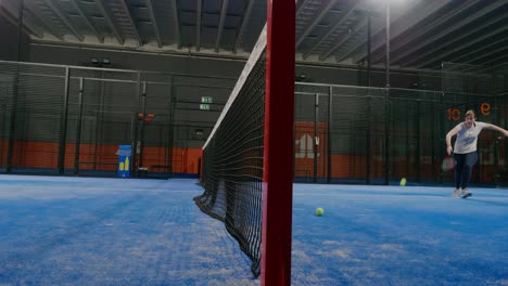 Pelota-De-Pádel-Volando-Sobre-La-Cancha-Interior-De-La-Red-De-Pádel-Y-Una-Mujer-Joven-La-Atrapa---Tiro-Ancho-Estático