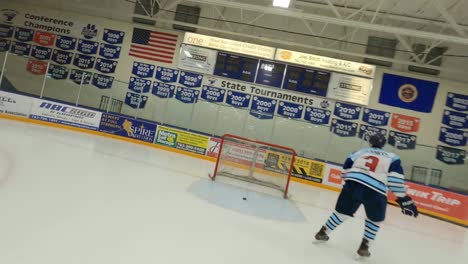 FPV-drone,-ice-hockey-player-skating-down-arena-rink,-shooting-puck-into-goal