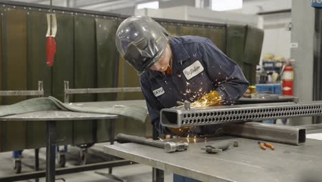 Man-with-face-shield-up-welding-piece-of-metal-in-factory-workshop