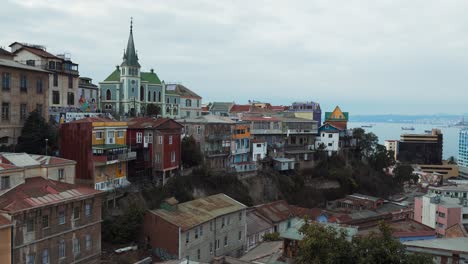Pan-right-of-colorful-hillside-houses-and-Lutheran-church-from-Cerro-Alegre-in-Valparaiso-city,-sea-in-background,-Chile