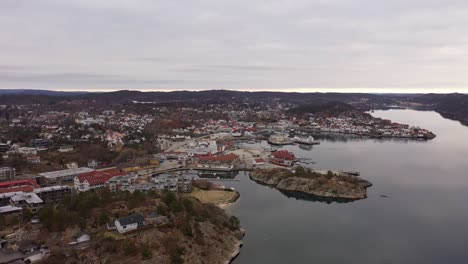 Aerial-approaching-Grimstad-city-above-sea-with-soft-reflections-during-morning---Wooden-white-houses-and-marina-in-southern-Norway-archipelago