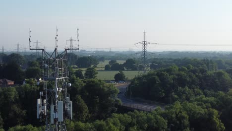 Aerial-view-5G-broadcasting-tower-antenna-in-British-countryside-with-vehicles-travelling-on-highway-background-rising-right