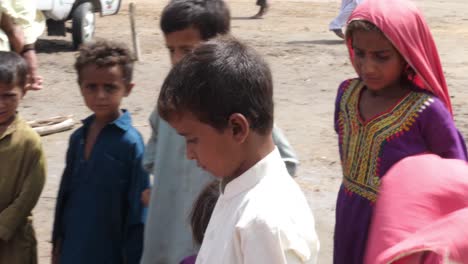 Un-Grupo-De-Niños-Sentados-Y-Jugando-En-El-Suelo-Polvoriento-Frente-Al-Campamento-De-Ayuda-Contra-Inundaciones-En-Sindh,-Pakistán
