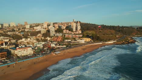 Aerial-view-dolly-right-flying-above-Reñaca-golden-Chile-scenic-sandy-beach-waterfront-ocean-waves