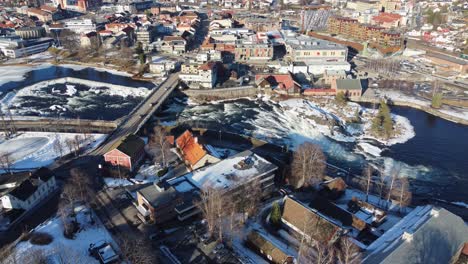 Kongsberg-bridge-and-river-in-city-center-during-beautiful-sunny-winter-day---Aerial-looking-down-at-city-while-slowly-descending-and-tilting-up---Norway
