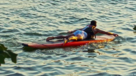 Mann-Liegt-Auf-Dem-Paddelbrett-Und-Schwimmt-Während-Der-Goldenen-Stunde-In-Zeitlupe