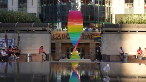Canary-Wharf-London-England-June-2022-Pride-tribute-sculpture-slow-motion-rotating-by-the-Cabot-Square-fountain-with-the-reflection-playing-back-across-the-water