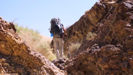 Static-shot-of-alone-hiker-with-a-hiking-pack,-going-around-Crater-Ramon,-Negev-desert-in-Israel-on-a-bright-sunny-day
