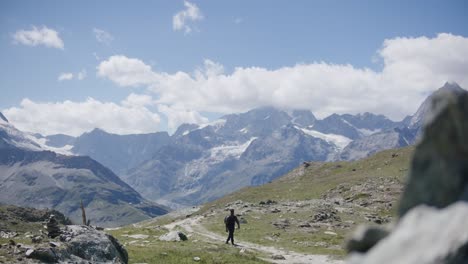 Black-male-traveler-with-backpack-walking-from-cliffside-exploring-the-mountain-landscape-near-the-Matterhorn-in-Switzerland
