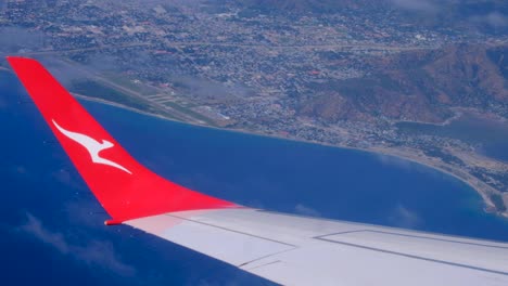 Qantas-plane-with-kangaroo-logo-on-wing,-flight-arriving-in-Dili-Timor-Leste-from-Darwin-Australia-with-a-view-of-the-country-coastline-and-ocean-from-airplane-window