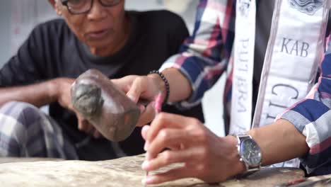 Elderly-Old-man-is-showing-how-to-create-shadow-Puppets-or-wayang-kulit-using-hammer-and-nails-to-the-young-man-beside-him-or-Putera-Pariwisata-Jawa-Barat,-then-try-it