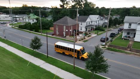 Public-school-bus-drives-through-town-community-in-USA-past-American-flag