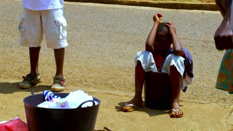 Child-sites-in-a-water-bucket-by-the-public-borehole-while-his-mother-does-laundry-by-hand