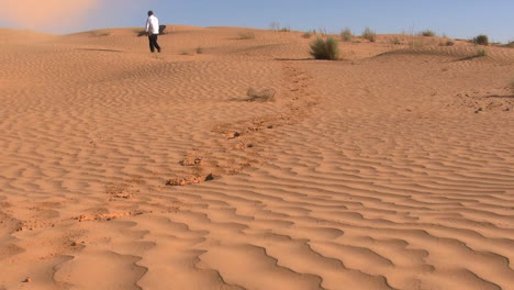 Man-is-walking-through-the-dessert,-small-sand-storm-is-whistling-near-him