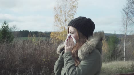 Adult-girl-walking-and-feeling-sick-blowing-her-nose-to-the-tissue-in-cold-sunny-autumn-day