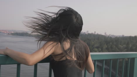 Medium-closeup-shot-of-asian-woman-running-and-climbing-on-railing-at-Lions-gate-bridge,-Vancouver-downtown-in-background,-Slowmo