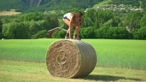 A-beautiful-brunette-woman-standing-up-and-balancing-carefully-on-a-large-bale-of-hay-on-a-farm-in-France