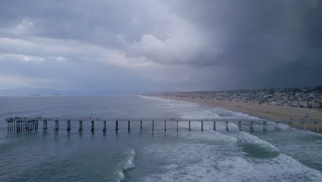 Stormy-landscape-of-waves-rolling-past-Manhattan-Beach-Pier,-California,-AERIAL-VIEW