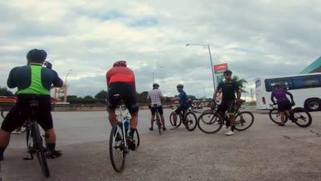 Un-Grupo-De-Ciclistas-Reunidos-En-Una-Calle-Frente-A-Una-Gasolinera