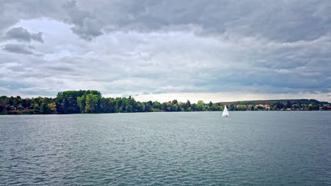 Sailboat-in-a-German-lake-with-trees-in-the-background-and-an-impressive-sky,-4k