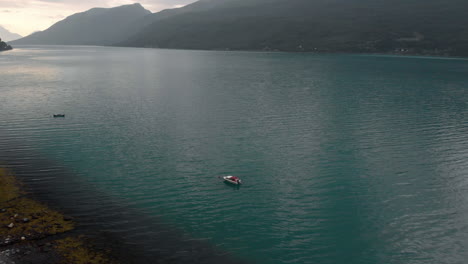 Ein-Kleines-Boot,-Das-Im-Wunderschönen-Türkisfarbenen-Meer-Schwimmt,-Umgeben-Von-Bergen