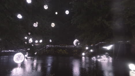 Verschwommene-Weihnachtslichtkugeln-Schmücken-Einen-Teich-In-Einem-Park,-Regnerische-Nacht