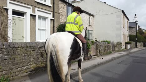 Female-in-rural-English-village-riding-horse-through-village-street