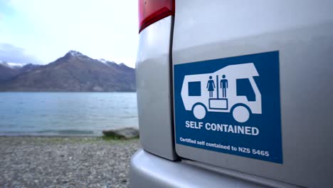 SLOWMO---Self-contained-motorhome-by-beautiful-blue-Lake-Wakatipu,-Queenstown,-New-Zealand-with-mountains-fresh-snow-cloudy-sky-in-background