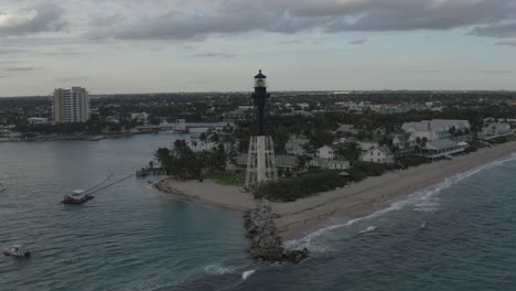 Aerial-shot-orbiting-a-lighthouse-showing-its-surrounding-bay,-ocean-and-buildings