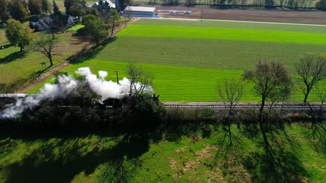 Tren-De-Pasajeros-De-Vapor-Echando-Humo-A-Lo-Largo-De-La-Campiña-Amish-Visto-Por-Un-Dron