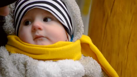 Caucasian-baby-boy-with-a-yellow-scarf-looking-around-and-at-his-mother-outdoors,-CLOSEUP