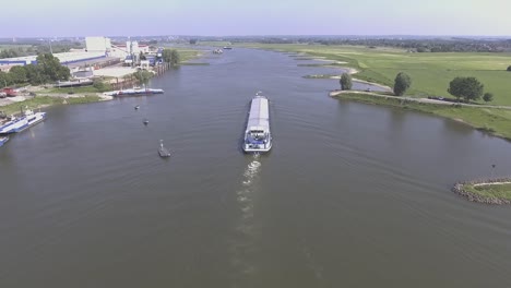 A-drone-shot-flying-forward,-flying-over-a-river-while-following-a-cargo-ship-in-the-Netherlands