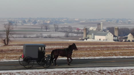 Drone-following-an-Amish-man-driving-his-buggy-with-a-horse-on-a-road-in-Intercourse,-Pennsylvania