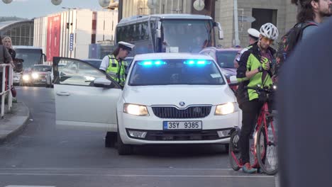 Police-car-with-blue-lights,-police-officers-and-people-crossing-street