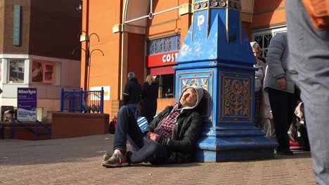 A-homeless-man-asleep-in-the-city-centre-people-just-walking-by-outside-the-biggest-shopping-centre-in-the-city,-Intu-Potteries