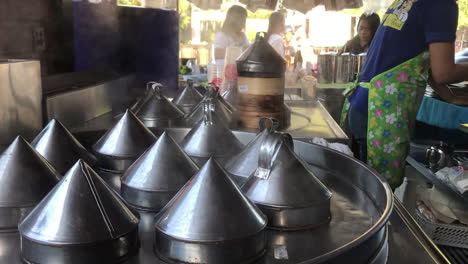 hand-held-shot-of-freshly-steaming-dim-sum-tin-steel-pots-in-a-food-stall-and-roadside-restaurant-in-Rawai,-Phuket,-Thailand