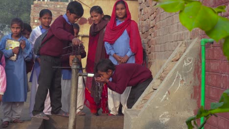 A-Pakistani-school-children-from-rural-area-drinking-water-by-hands-and-a-glass-by-a-hand-pump,-In-winter`s-season,-wearing-sweaters-and-jackets,-Fun-and-smiling