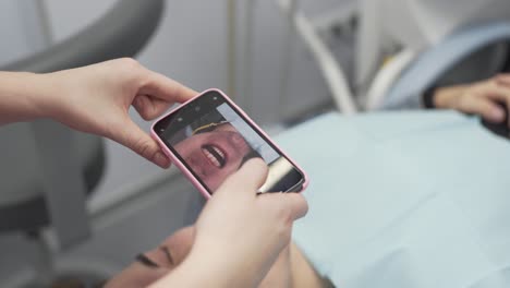 Dentist-in-Modern-Dental-Clinic-Uses-Her-Mobile-Phone-Camera-to-Take-Pictures-of-Teeth-of-Her-Male-Patient-After-Successful-Treatment