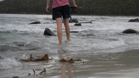 Slow-Motion-Of-Person-In-Shorts-Walking-Into-Water-With-Rocks-And-Rolling-Waves,-Tasmania,-Australia