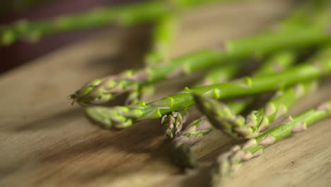 Slow-motion-footage-of-a-bunch-of-fresh,-green-asparagus-falling-on-to-a-wood-cutting-board