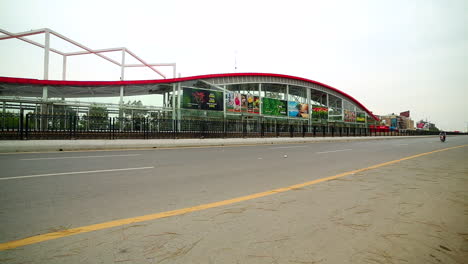 Low-angle-view-of-a-metro-bus-station-from-the-corner-of-the-road,-A-white-car-and-two-motor-bikes-going-on-the-road