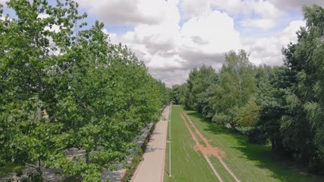 A-flight-near-the-trees-above-the-bike-path,-green-space-in-a-safe-place-with-lanterns-and-a-sidewalk,-a-place-to-rest-outside-the-city,-aerial-shot-in-4k