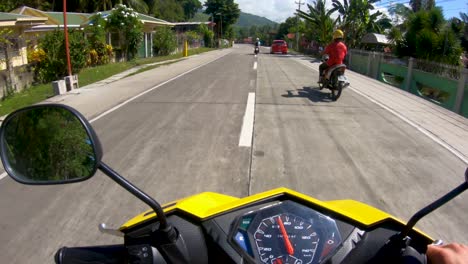 A-smooth-panning-shot-of-a-man-riding-a-motorcycle-along-a-beautiful-sunny-coastal-road-on-the-island-of-Bohol,-Philippines