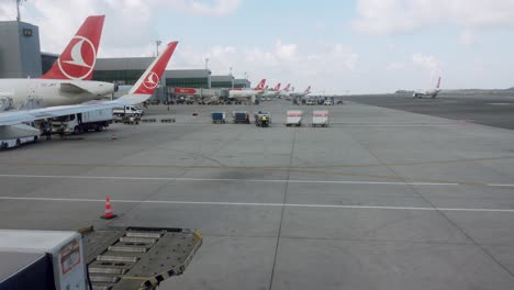 View-on-busy-workers-in-the-airport,-handling-luggage-carts---lot-of-planes-in-row