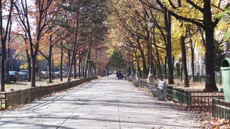 Bukarest,-Rumänien-9.-November:-An-Einem-Herbsttag-Im-Park-Auf-Dem-Bürgersteig-Spazieren-Gehen,-Mit-Menschen-Herum-Und-Die-Sonne-Spiegelt-Sich-Auf-Den-Gebäuden-Und-Blättern,-Die-Von-Den-Bäumen-Gefallen-Sind